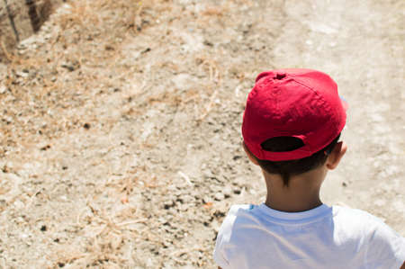 Boy with red cap walking on a sand and gravel road.
