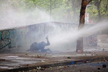 Santiago, Chile - October 06, 2011: A demonstrator falls after he was hit by a jet of water during a student strike in Santiago's Downtown, Chile. Protesters demand the government to improve education quality.のeditorial素材