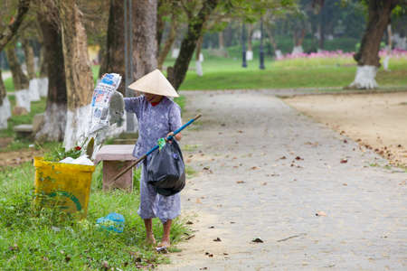 HUE, VIETNAM - MARCH 7: Old woman collects stuff from garbage in public park on March 7, 2014 in Hue, Vietnam.のeditorial素材