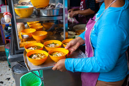 IPOH, MALAYSIA - DECEMBER 11: Woman serves up chicken soup for clients on a food court of Ipoh on December 11, 2018 in Ipoh, Malaysia.のeditorial素材