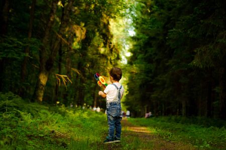 Cute little blond boy with a toy in the forest road.の写真素材