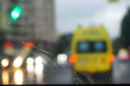 Defocused image of emergency ambulance travels through city street seeing through the wet from rain wind screen of a car.の写真素材