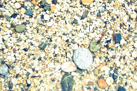 Macro close up of coarse rice-sized multi-coloured wet shiny sand grains and gravel texture, top...