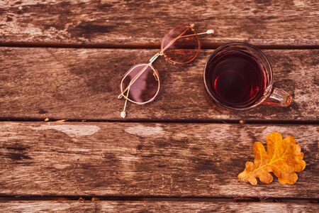 Cozy autumn tea break with a cup of tea , sunglasses, and dry autumn leaves on old vintage wooden table. top down view.の写真素材