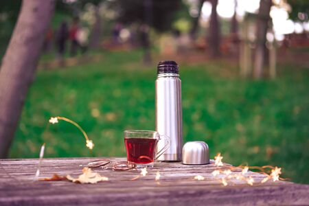 Cozy autumn tea break with a cup of tea , thermal flask,sunglasses, and dry autumn leaves on old vintage wooden table. top down view.の写真素材