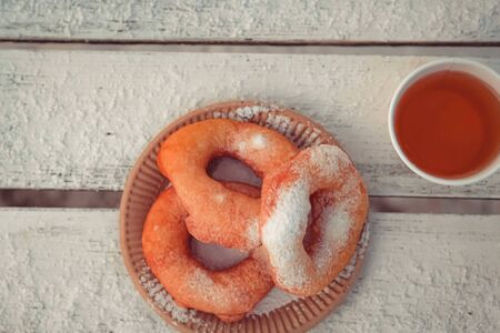 Russian fast food bagel pyshki and paper cup with tea or coffe on wooden table, covered with snow, winter snack in the park.の写真素材