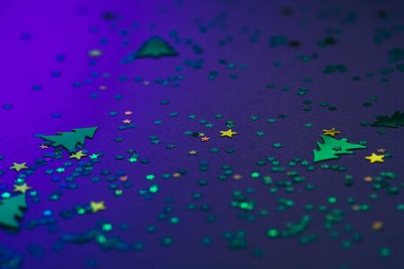 Christmas frame composition with golden star-shaped sequins and pine trees on blue holographic background. Celebration preparation concept. Selective focus.の写真素材