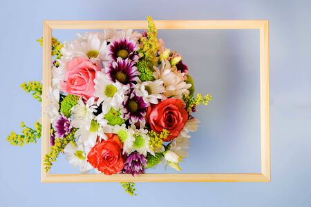Bouquet of roses and daisies on light blue background with wooden frame and space for text. Top view. Event concept.の写真素材