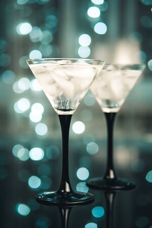 Couple of cocktail glasses with a dring with ice on trendy black background with bokeh lights. Evening or night party concept.の写真素材