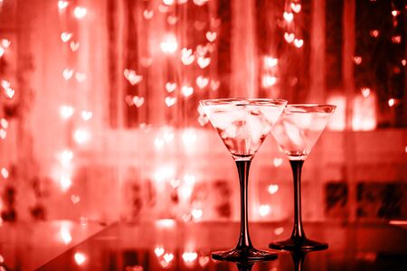 Couple of cocktail glasses with martini drink with ice on trendy black background with bokeh lights. Evening or night date concept. Toned red.の写真素材