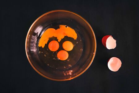 Raw crashed eggs in glass bowl on black backgroundの写真素材