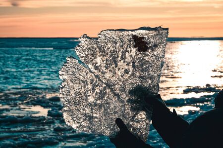 Cropped image of a man, holding a large piece of ice on sunset sky and lake background . End of winter, spring is coming concept.の写真素材