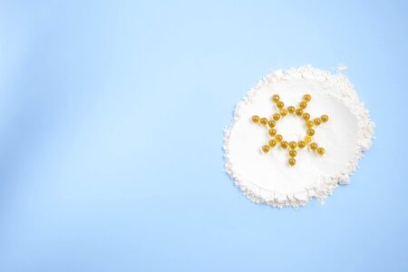 Vitamin D yellow pills in the shape of sun on white lecitin powder in sky blue background, nutrition supplements concept.の写真素材