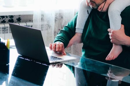 Cropped image of a busy businessman wearing pijamas working from home and watching a child, sitting on his shoulders. Home office and distant education concept. Father and son.の写真素材