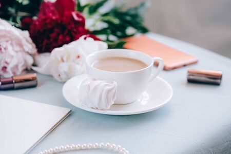 Morning coffee with flowers, cell phone, notebook and some feminine accessories. Modern womans morning concept.の写真素材