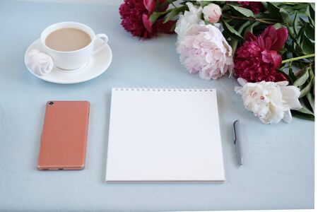 Notebook and a cup of coffee on blue fabric backgroundand peony flowers and cell phone. Feminine morning concept.nの写真素材
