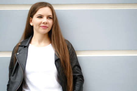 Young woman with long hair standing at the wall of city building outside, . Girl in the city. Space...