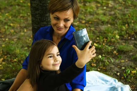 Mother and her little daughter taking selfie in the autumn park and having fun.