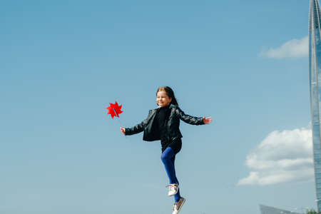 Happy girl with red wind spinner walking on the embankment on blue sky urban background. Freedom conceptの写真素材