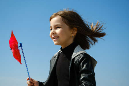 Happy girl with red wind spinner walking on the embankment on blue sky urban background. Freedom conceptの写真素材