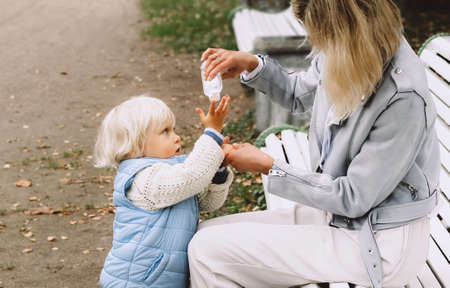 Mother applies sanitizer for cleaning her sons hands in public place. New normal, resilience...