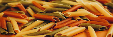 Frame made of colorful green, yellow and red penne pasta naturally coloured with tomato and spinach. Non-perishable products concept. Web bannerの写真素材