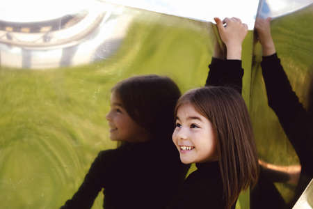 Little girl in stylish autumn black outfit in an urban setting . Reflective mirror background.の写真素材