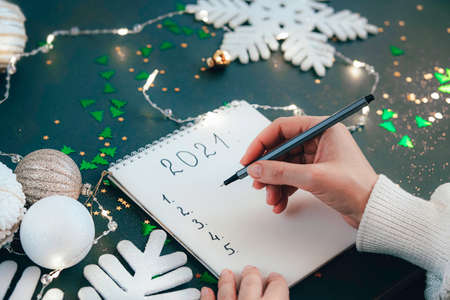 New Years goals. Year 2021. Womans hand writing the list in a notepad. Resolution Aspirations...