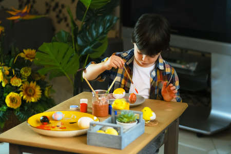 Little boy painting wooden eggs for Easter decoration. Candid image of kids crafting.