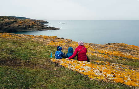 Woman and two kids wearing winter clothes sitting on the mountain shore looking at the Bosphorous...