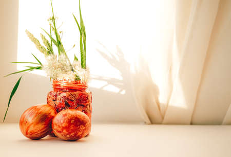 Red and gold Easter eggs and a bowl with fresh spring flowers on the window sill. Sunshine and shadow.の写真素材