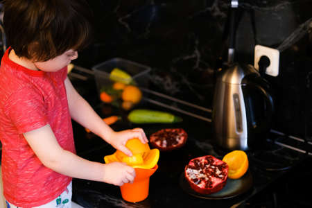Little boy making fresh orange juce squeezing oranges in the kitchen.の写真素材