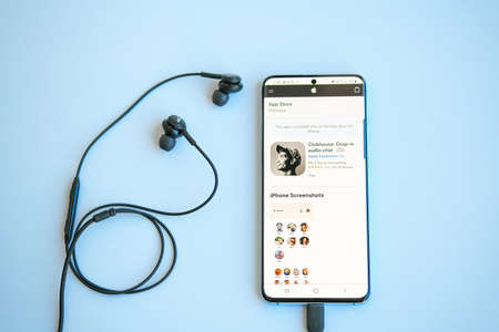 Saint-Petersburg, Russia - 02.17.2021: Clubhouse Apple application view on smartphone and white headphones on yellow and blue background.のeditorial素材