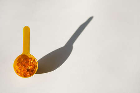 Yellow gel transparent gel capsules of vitamin d or omega 3 in spoon on gray background in sunlight.