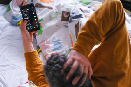 Mature man with his phone alarm clock in bed late for work and stressed.の写真素材