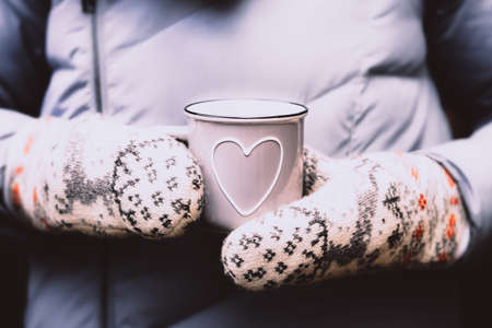 Hands in warm mittens holding gray cup with heartの写真素材