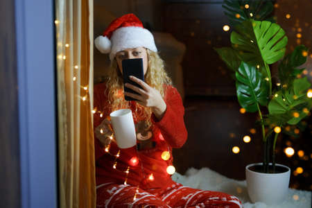 Happy woman in Santa hat and masquerade glasses with a glass of champane celebrating New Year's Eve...