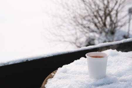 White paper cup with hot tea on snowy table.