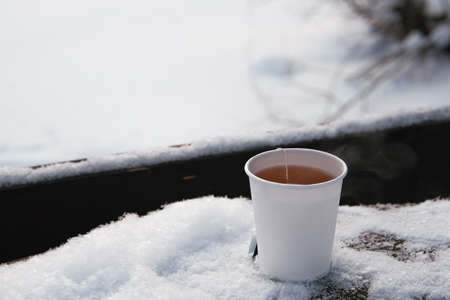 White paper cup with hot tea on snowy table.の写真素材