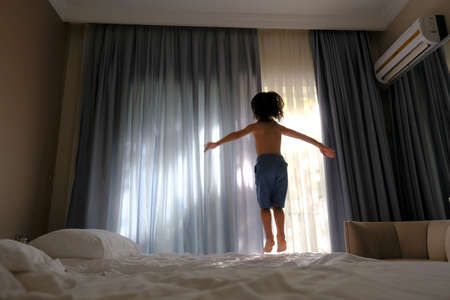 happy kid jumping on the bed with a phone listening to musicの写真素材