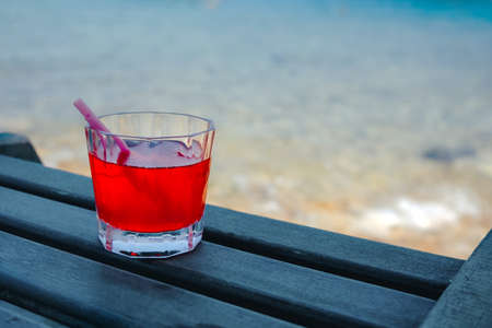 Red cocktail in a glass standing on wooden table at the beach cafe.