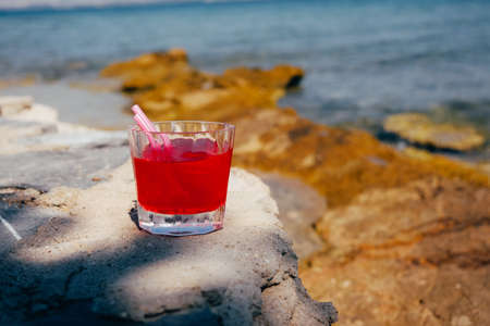 Red cocktail in a glass standing on wooden table at the beach cafe.の写真素材