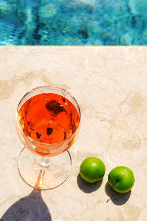 Glass of pink wine and yellow sunglasses at the pool.