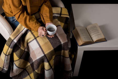 woman drinking coffee in an armchair next to a book.の写真素材