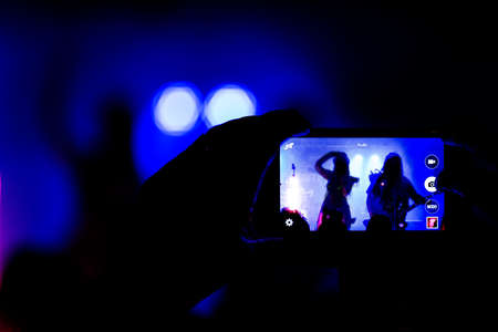 A girl takes a photo with his smartphone in a small club gig.の写真素材