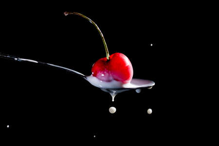 Splash of milk, caused by a fall of a cherry on a spoonの写真素材