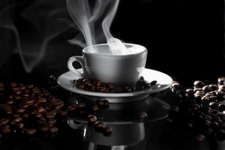 small white cup of steaming coffee on a black backgroundの写真素材