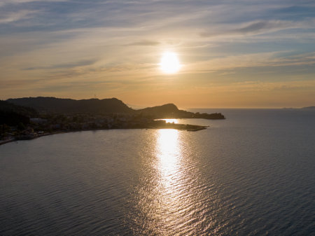 Sunset over tranquil coastal waters, with distant hills and warm hues.の写真素材