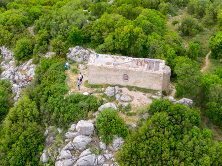 Aerial view of hikers by an old stone building amidst lush greenery.の写真素材