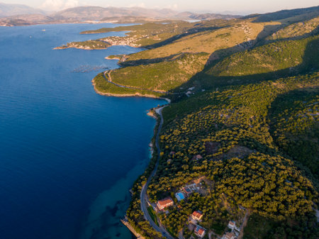 Aerial view of a coastal road winding through lush green hills, meeting the deep blue sea.の写真素材